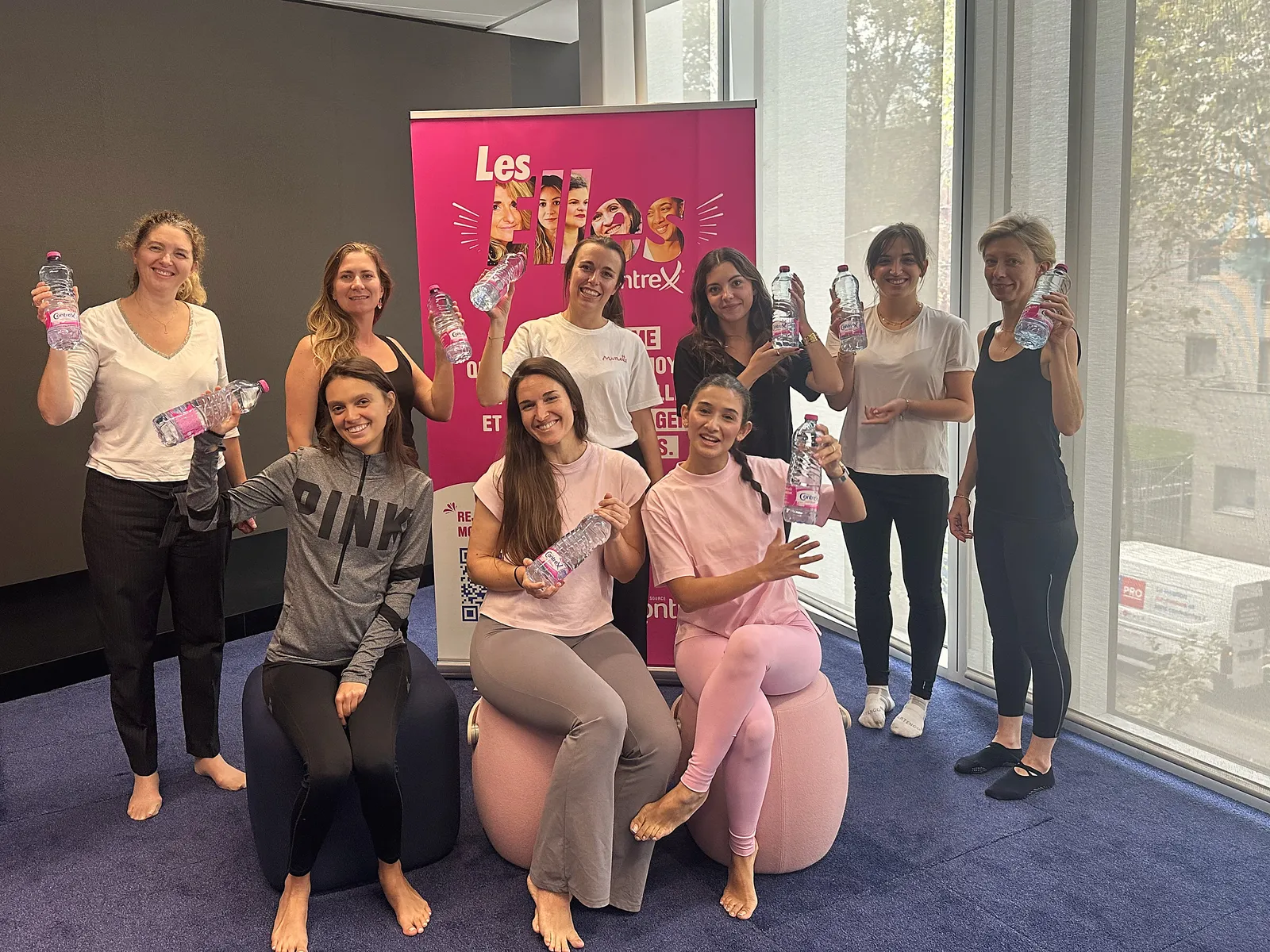 Photo de groupe après le cours de yoga Octobre Rose chez Nestlé Waters, bouteilles Contrex levées devant le kakémono Les Elles by Contrex